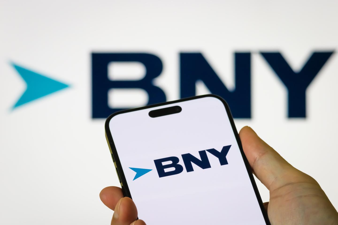A smartphone displaying the logo of The Bank of New York Mellon Corporation (BNY) in front of a BNY brand background.