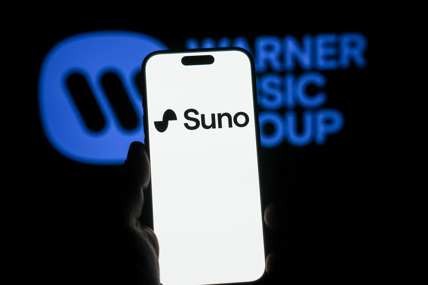 Suno Ai on a phone screen with Warner Music Group's logo in the background.