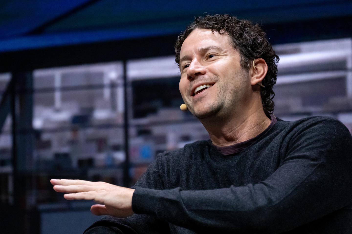 Daniel Nadler wears a black shirt, smiles, and speaks into an earpiece microphone