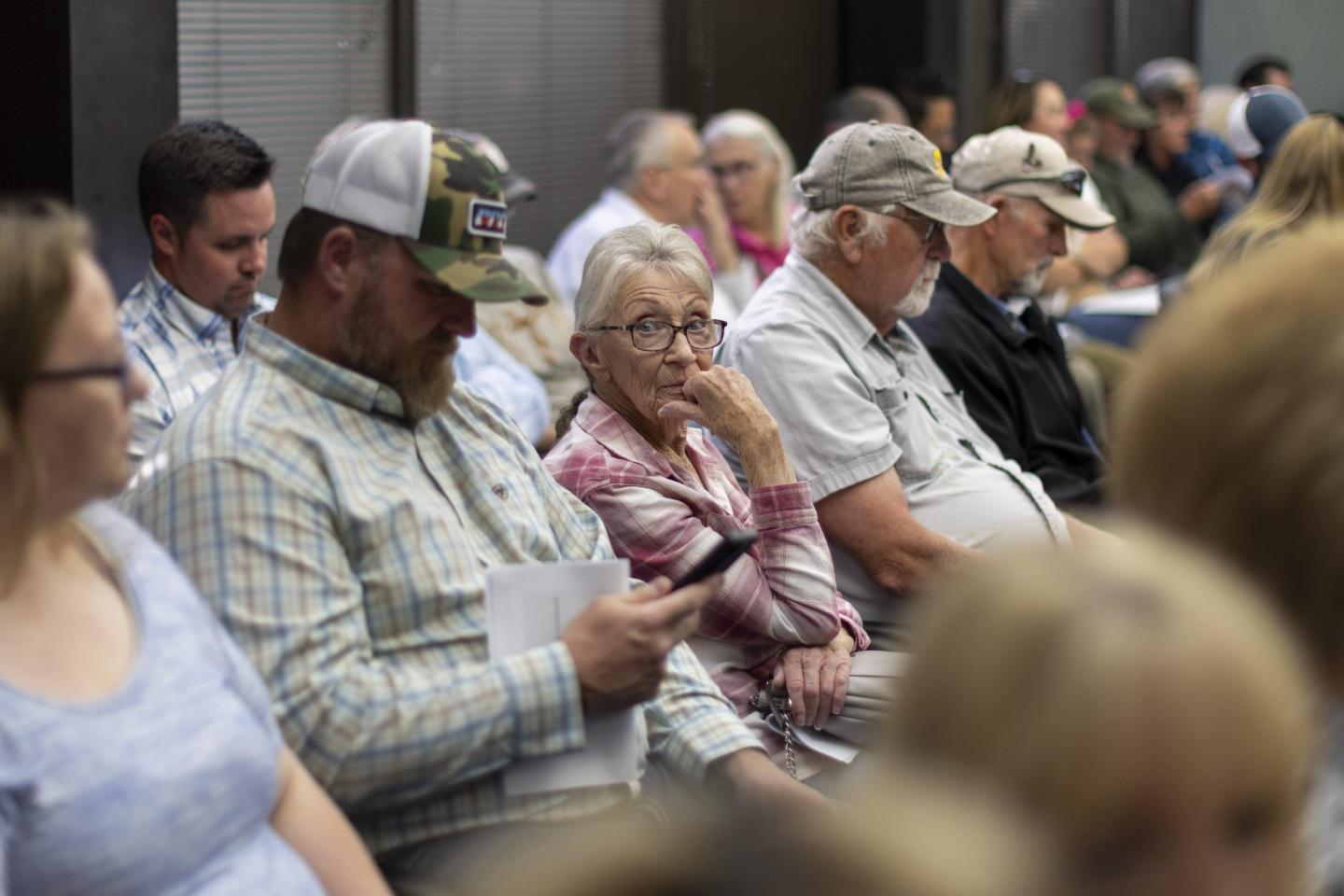 A row of people sit in a zoning meeting, many looking down or around the room.