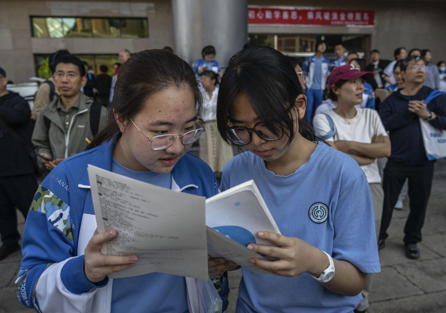 Two students stand next to each other and look at the papers they are holding.