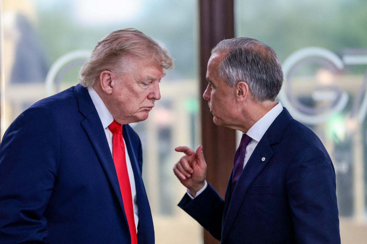 Canadian Prime Minister Mark Carney speaks to US President Donald Trump in front of a window.