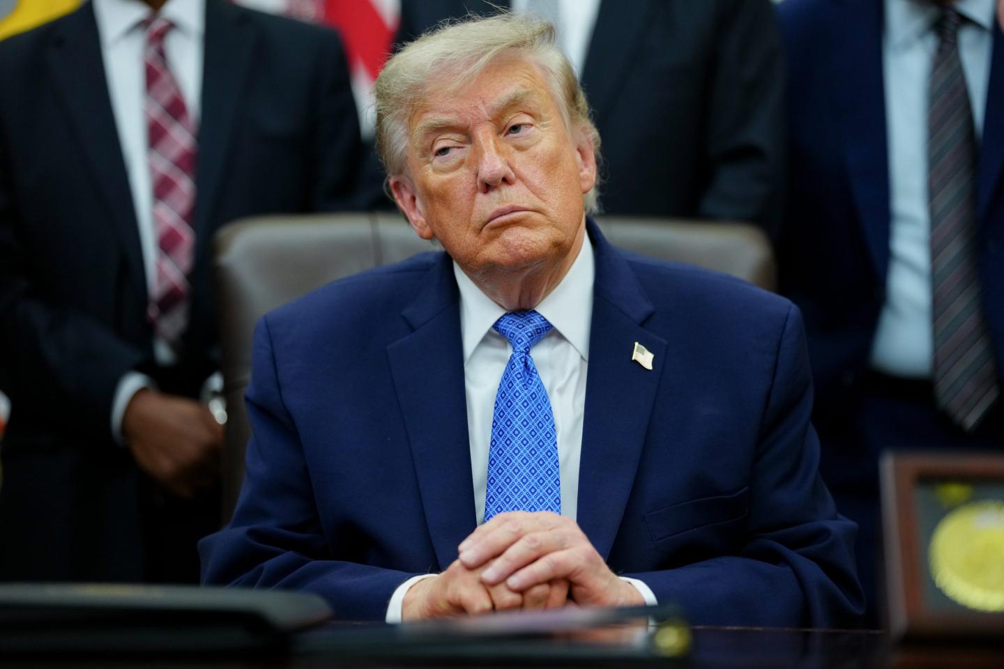 US President Donald Trump sits in silence with his hands folded on top of each other.