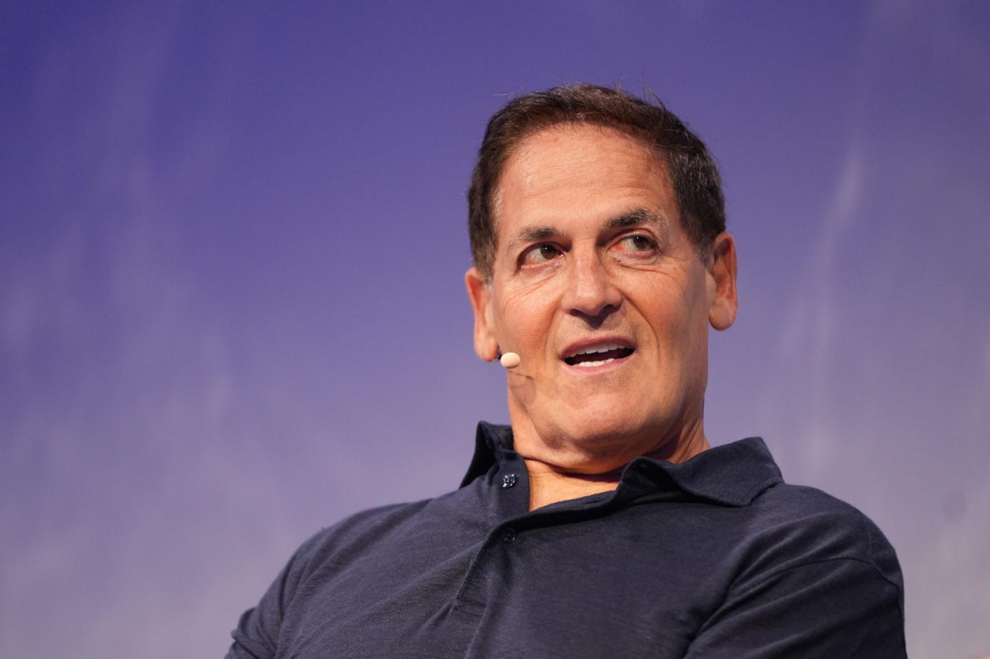 Mark Cuban, in front of a purple background, has his mouth open and is looking to his left.