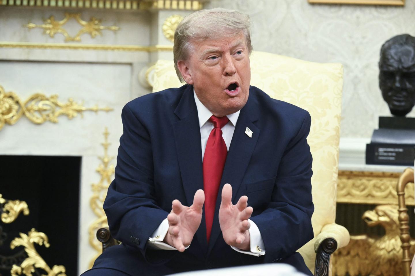 Trump sits in the Oval Office, speaking and gesturing with both his hands.