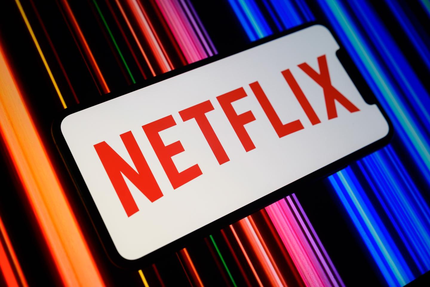 The Netflix logo is displayed on a smartphone screen featuring a color gradient in the background.