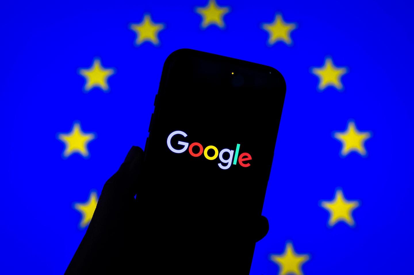Google logo is displayed on a smartphone in front of the EU Flag.