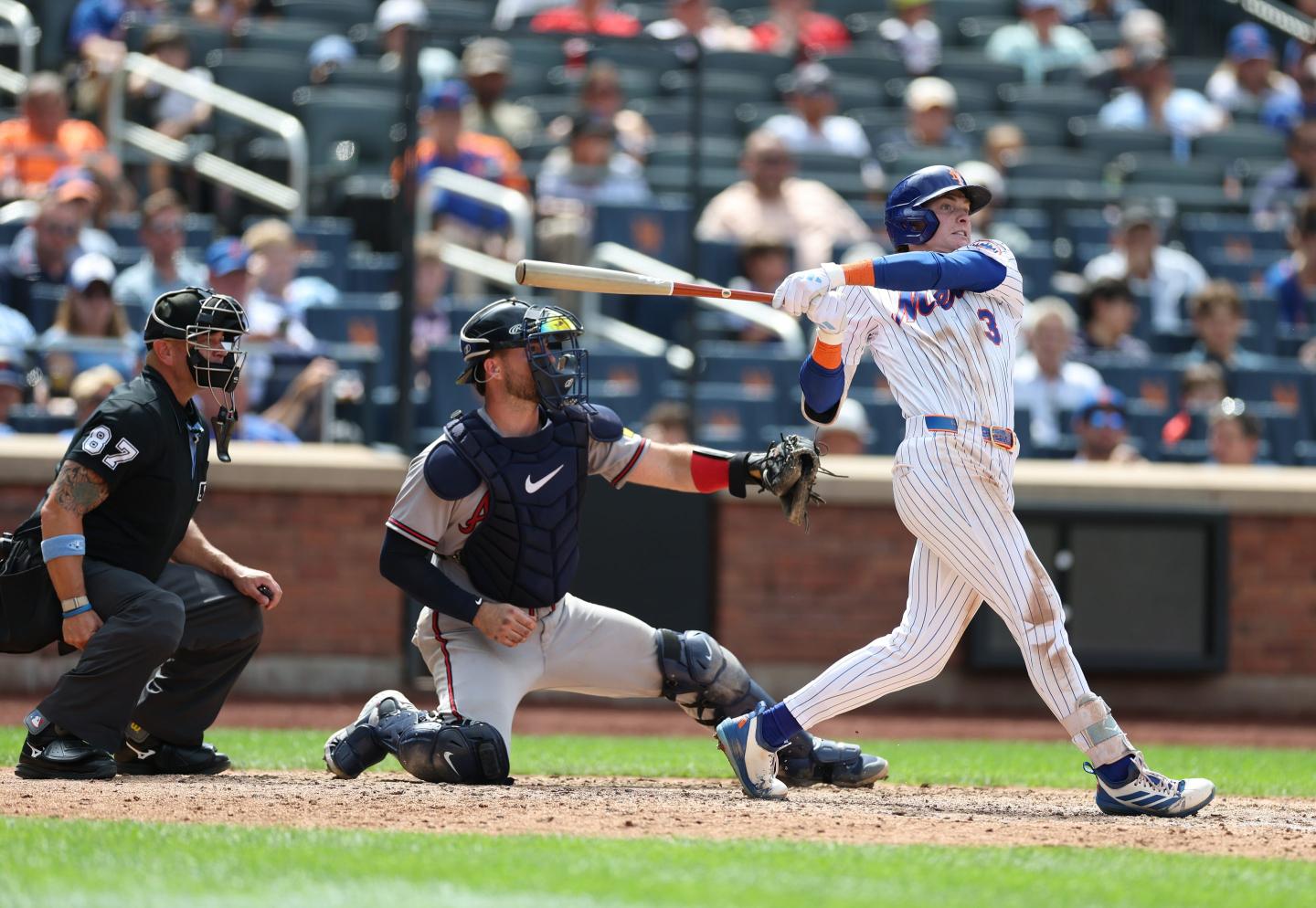 A baseball player swinging his bat with two umpires behind him.