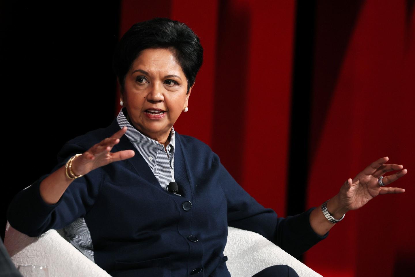 Indra Nooyi sitting in a chair behind a red background.