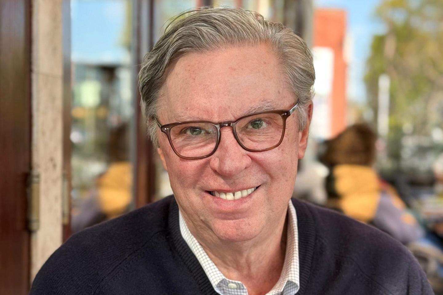White man glasses gray hair smiling.