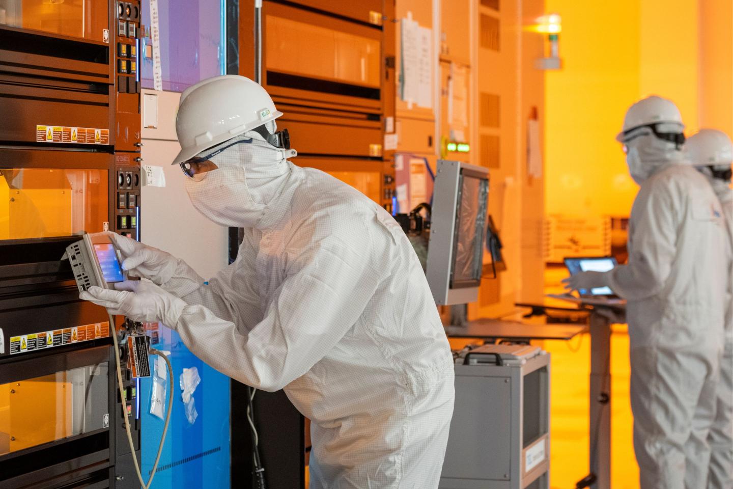 Worker in a full cleanroom suit uses a wafer manufacturing tool.