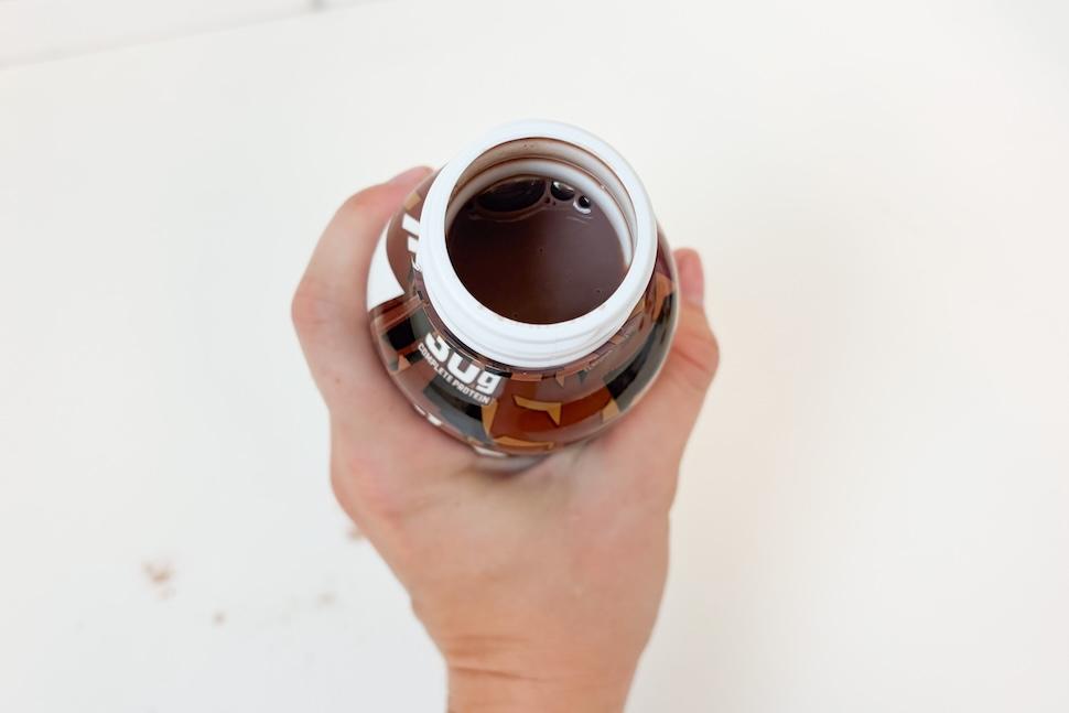 Closeup of a hand holding an open bottle of chocolate-flavored 1st Phorm Protein