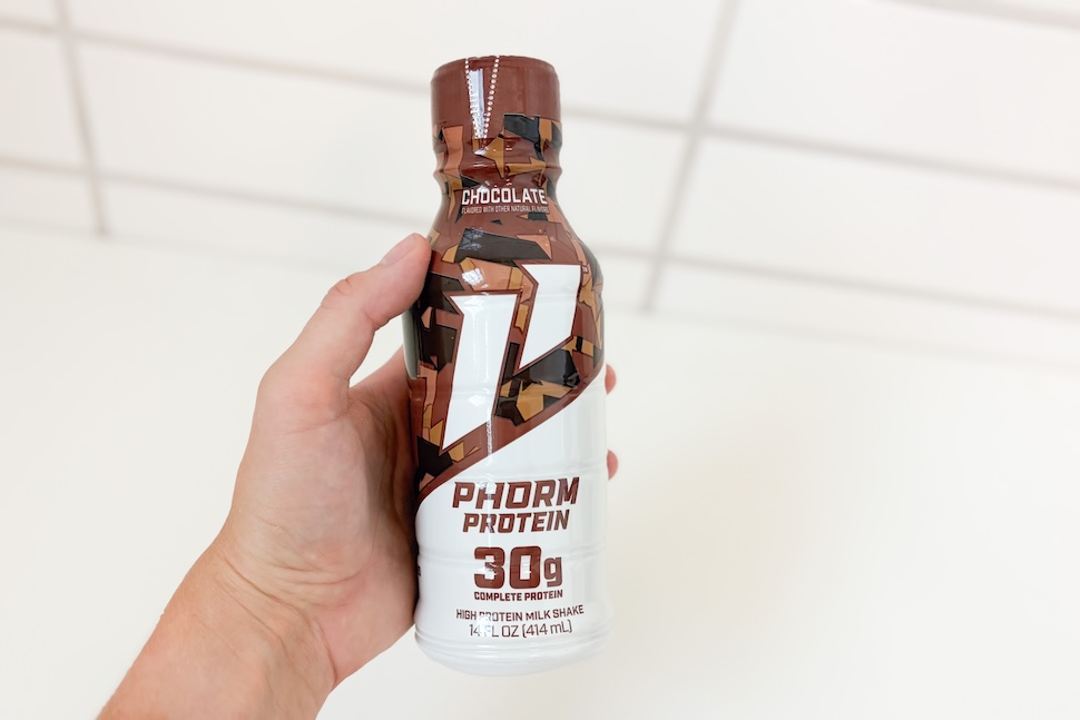 Closeup of a hand holding a bottle of chocolate-flavored 1st Phorm Protein