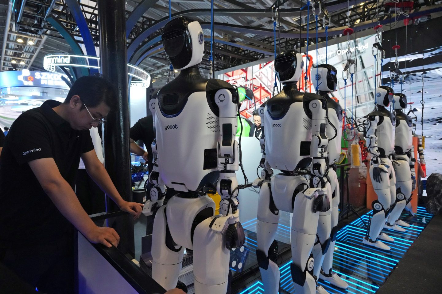 A worker reacts near a line of humanoid robots displayed at the World AI Conference in Shanghai.