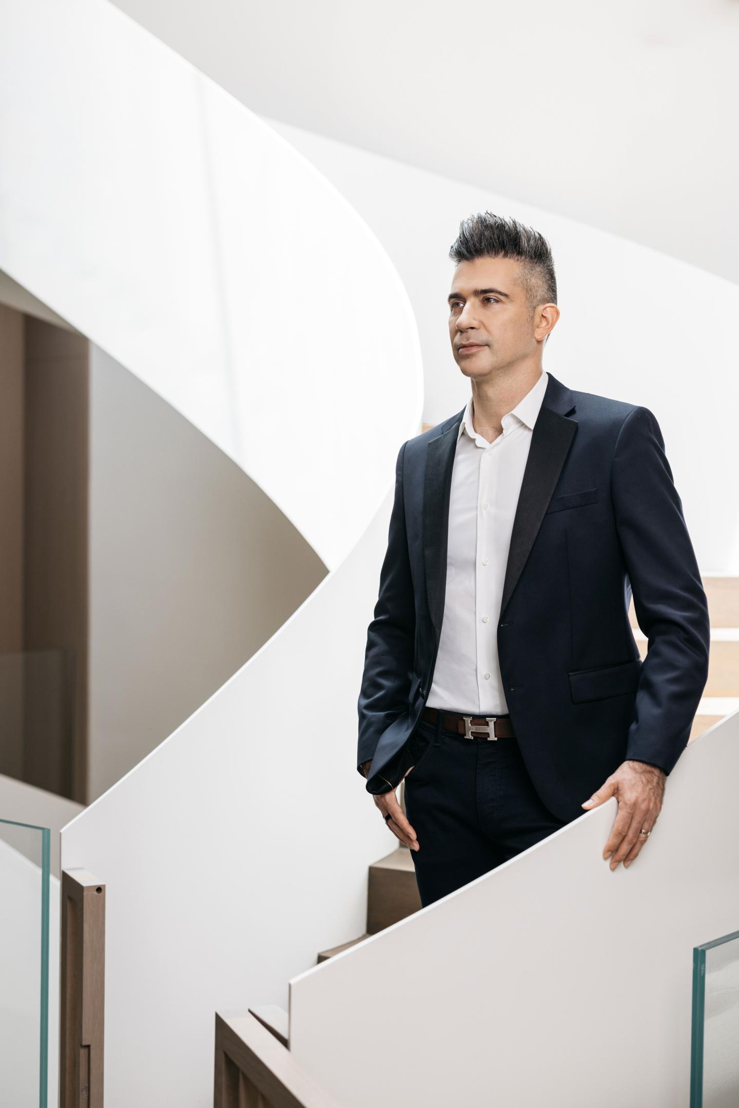 Yevgeny Dibrov wears a suit and stands on a white modern staircase
