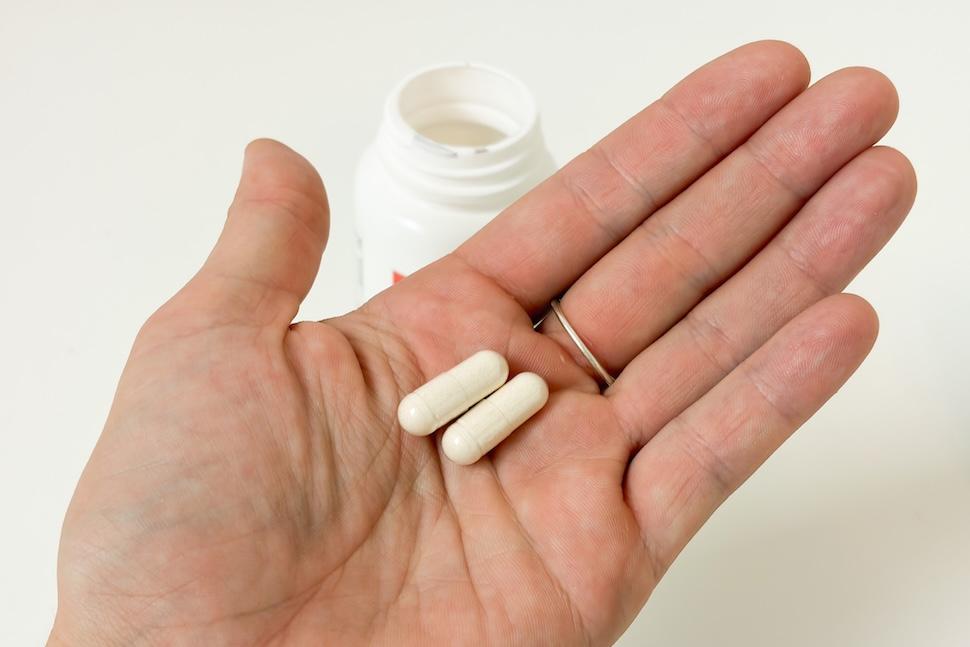 Closeup of an open palm holding two Performance Lab Caffeine 2 capsules. The capsules are off-white in color, and you can see the open pill bottle below on the countertop.