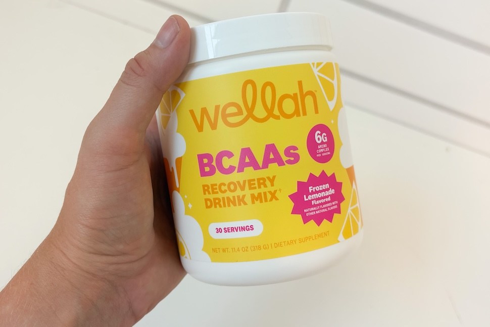 Closeup of a hand holding a canister of Wellah BCAAs