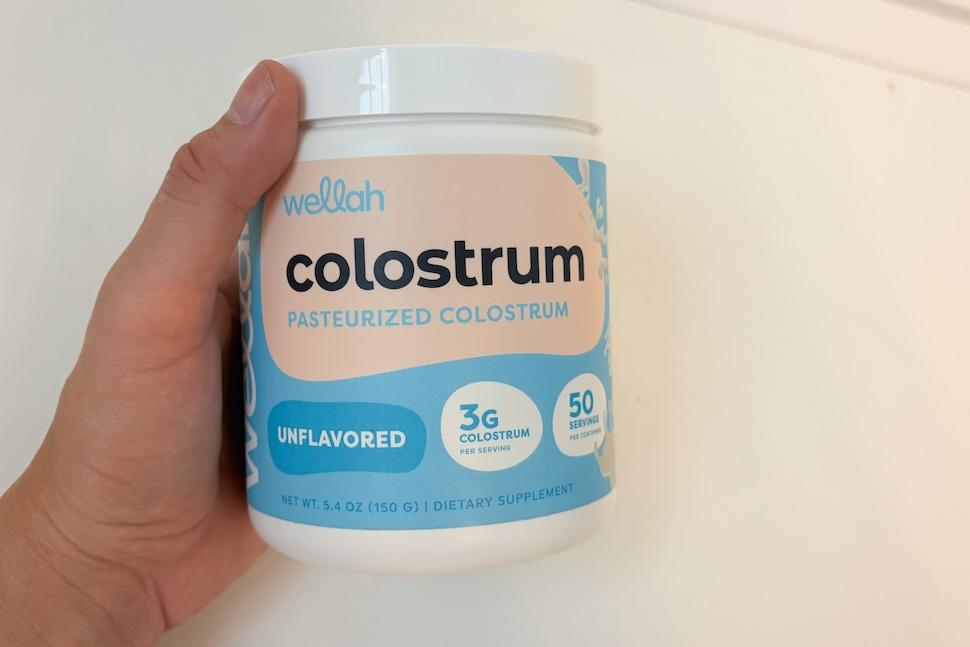 Closeup of a hand holding a canister of Wellah Colostrum