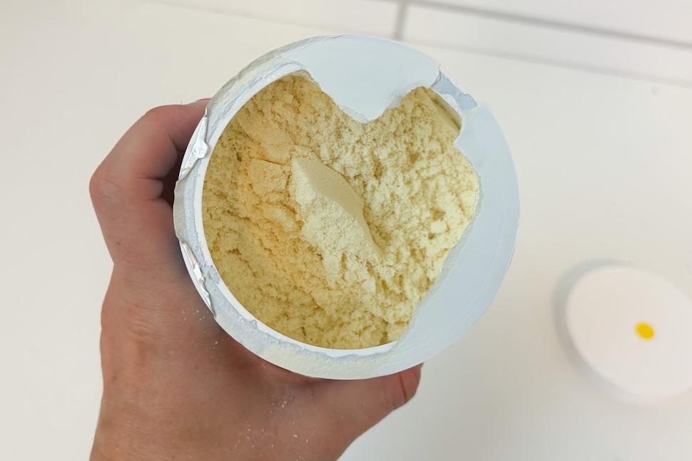 Closeup of a hand holding an open canister of Wellah Colostrum. Inside, you can see the fine, off-white powder.