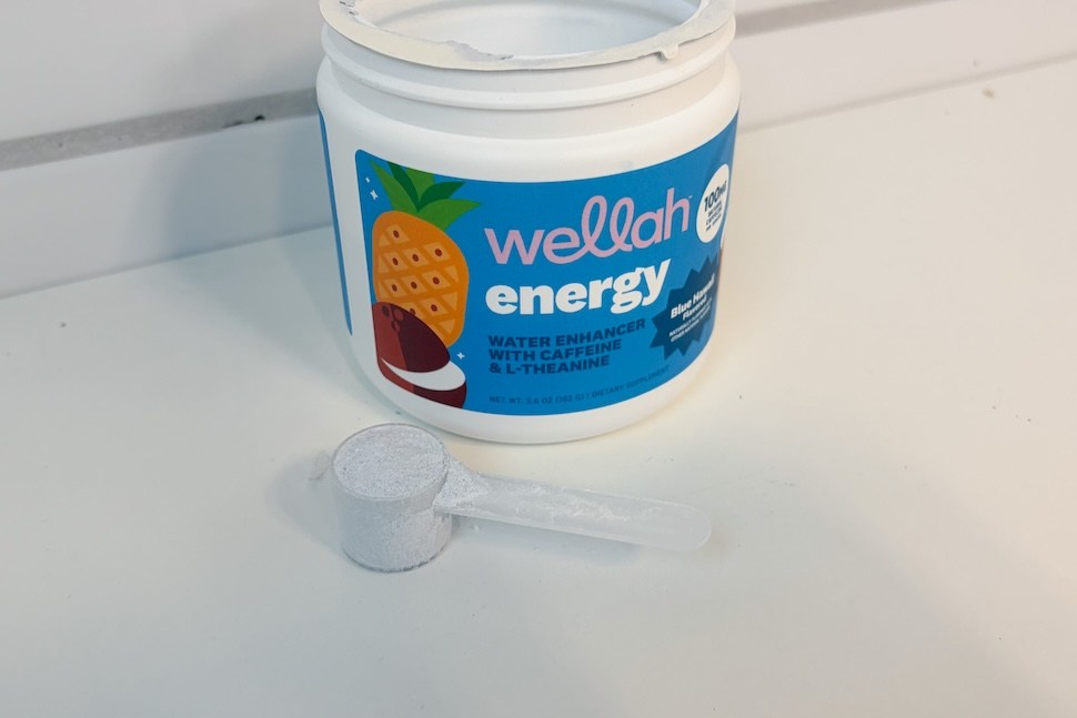 An open canister of Wellah Energy sitting on a white countertop. A plastic scoop rests next to it.