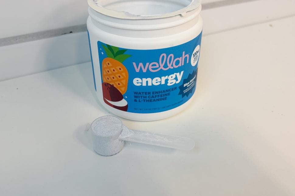 An open canister of Wellah Energy sitting on a white countertop. A plastic scoop rests next to it.
