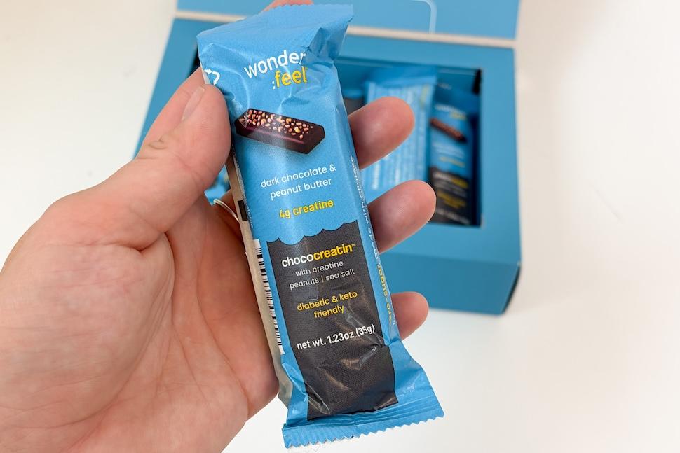 Closeup of a hand holding a Wonderfeel ChocoCreatin bar still in its blue wrapper
