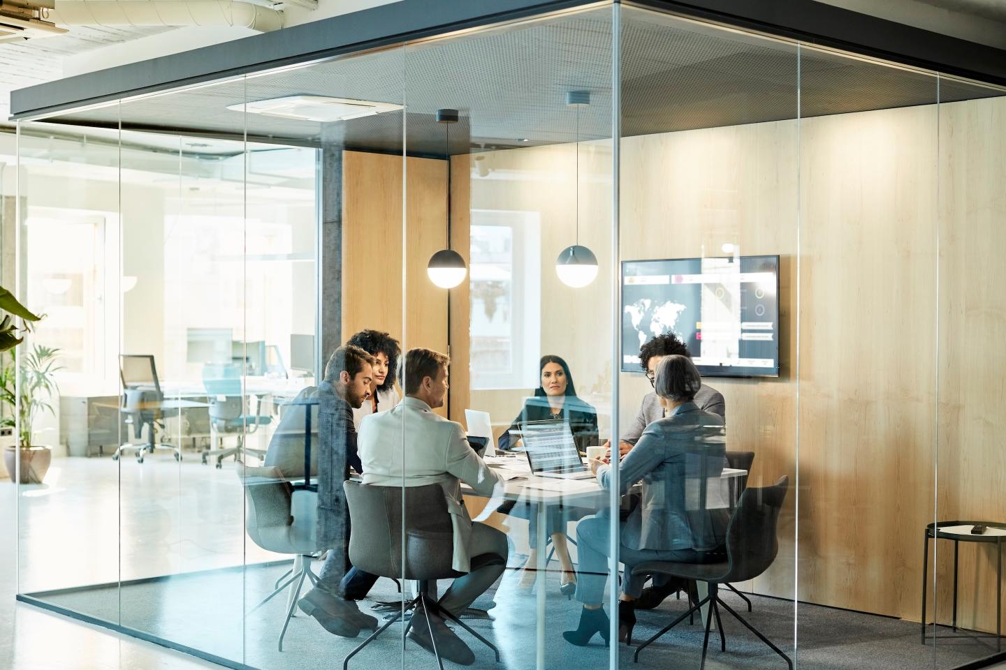 Business colleagues sitting at conference table seen through glass wall. They are planning strategy.