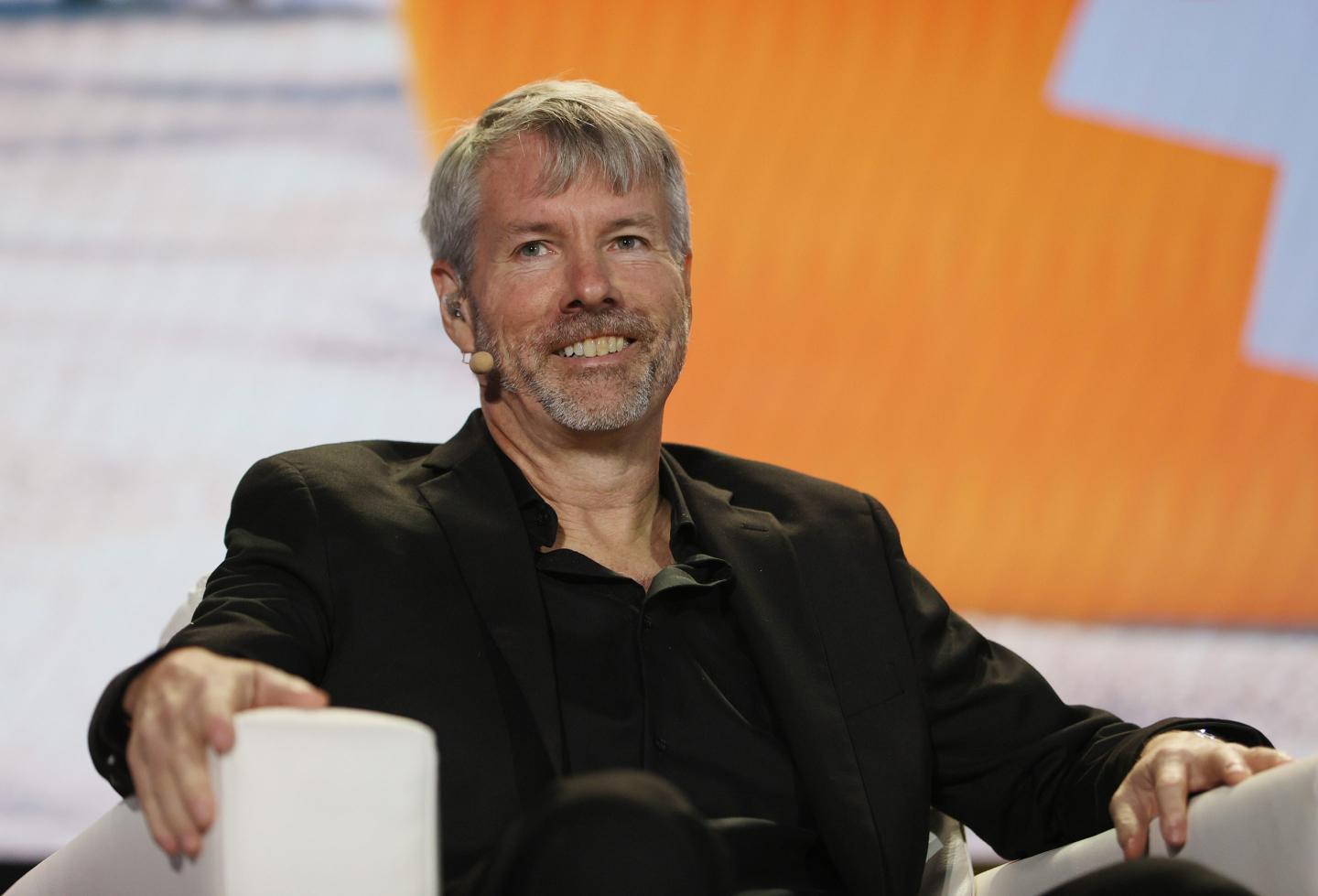 Michael Saylor sitting during a conference and smiling while looking into the distance.