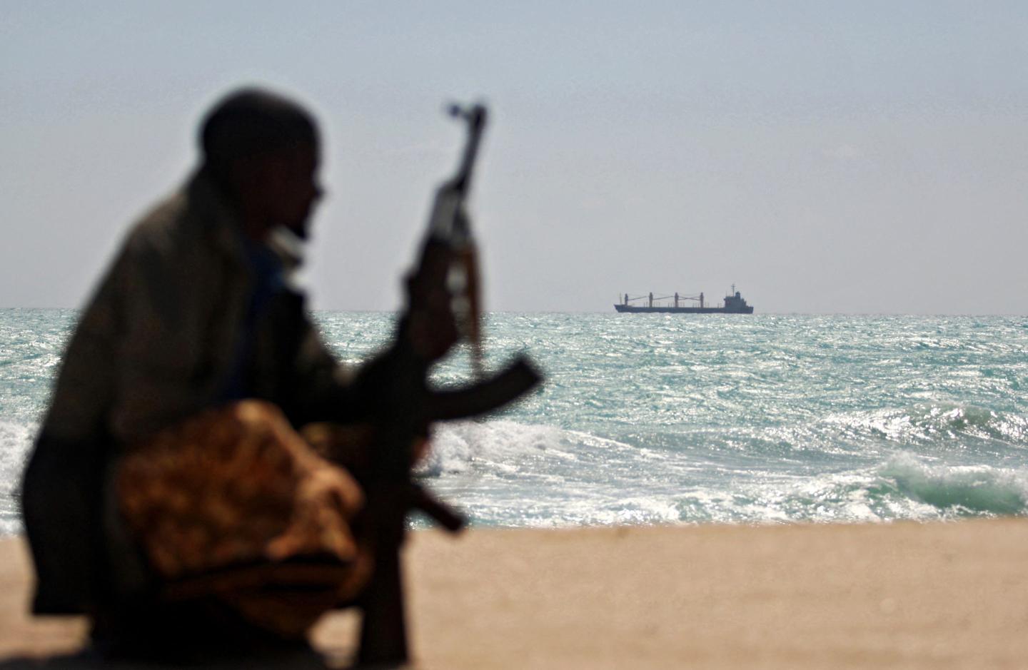 An armed Somali pirate along the coastline while the Greek cargo ship, MV Filitsa, is seen anchored just off the shores of Hobyo town in northeastern Somalia where its being held by pirates.