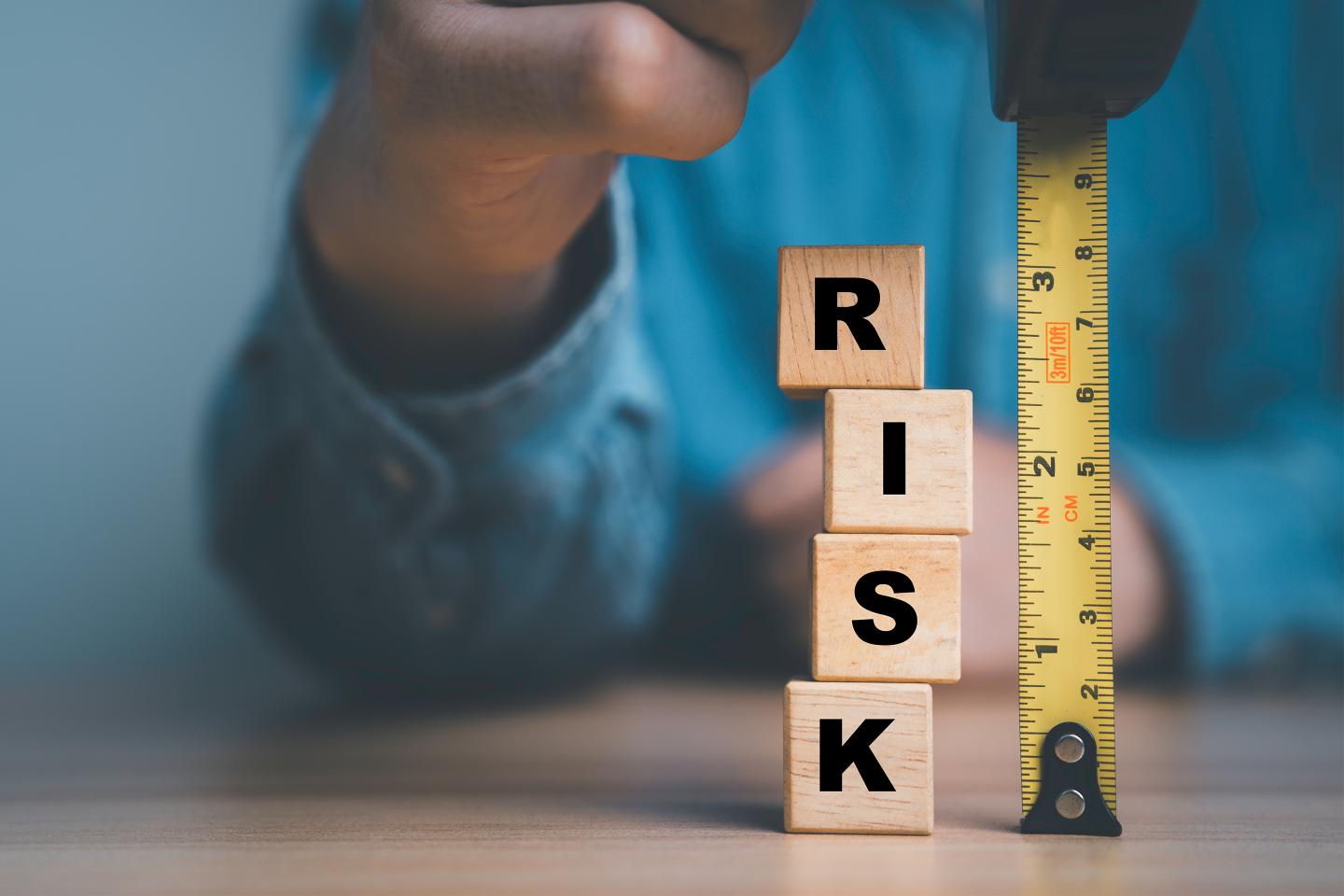 A stack of blocks spelling out risk next to a tape measure.