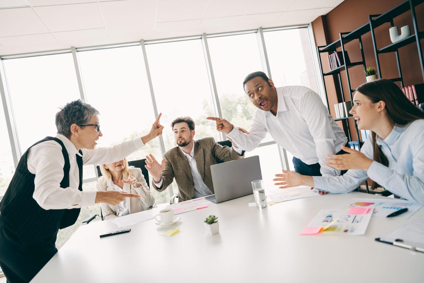 People pointing at each other in a boardroom.