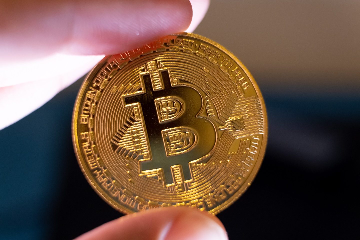 A physical Bitcoin coin held between an index finger and a thumb.