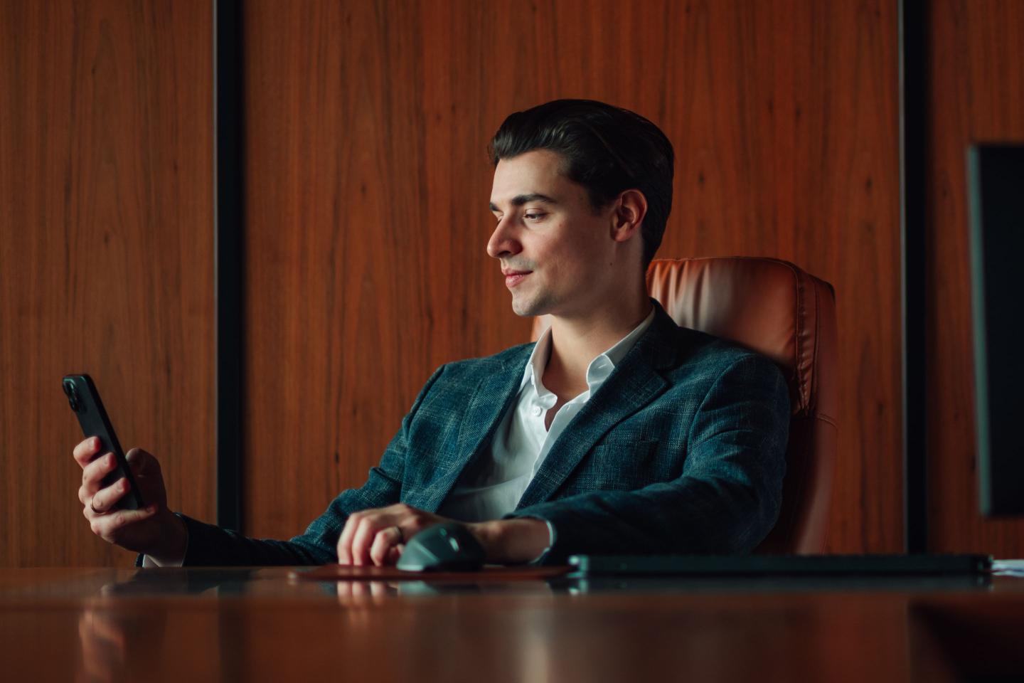 Young businessman checking smartphone in dark wood office
