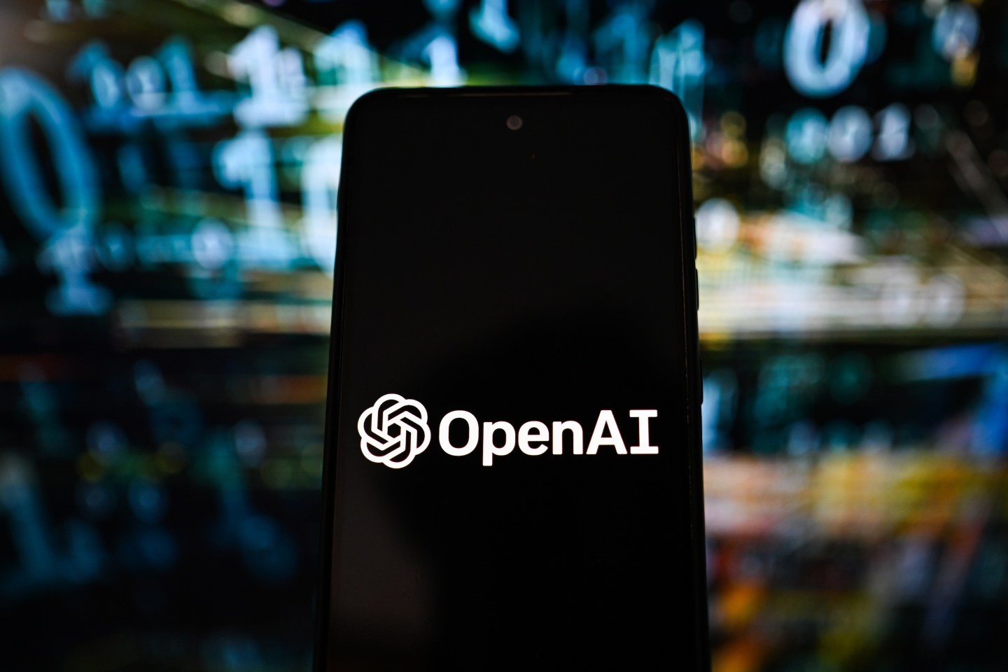 OpenAI logo is seen displayed on a smartphone with code in the background.