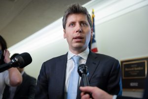 Sam Altman stands in front of microphones in a suit