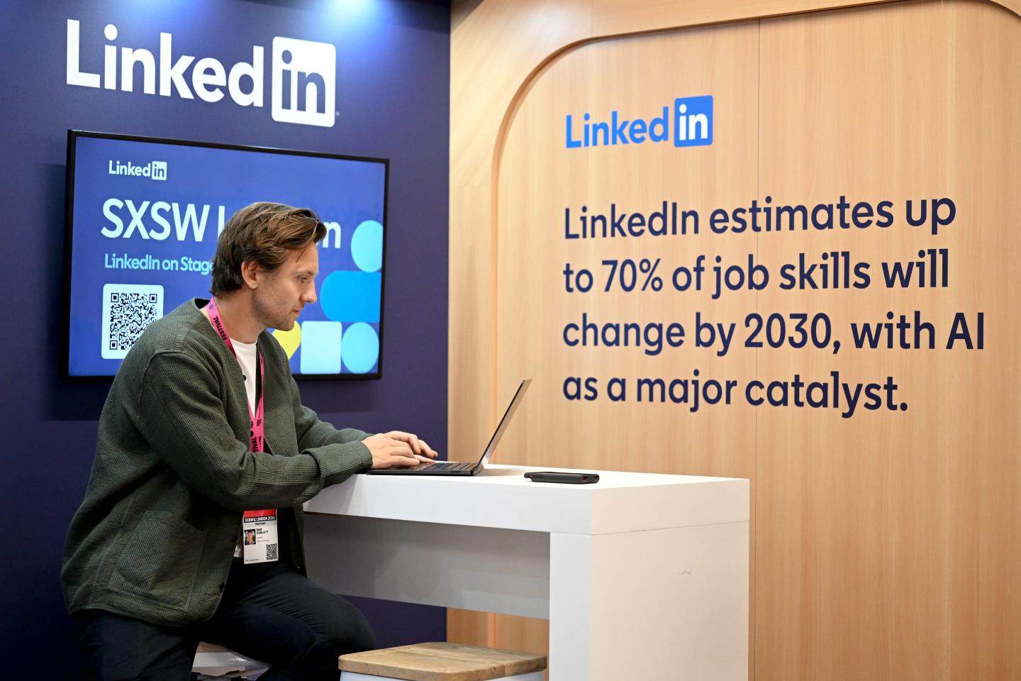 A man sits at a desk with a LinkedIn display behind him.