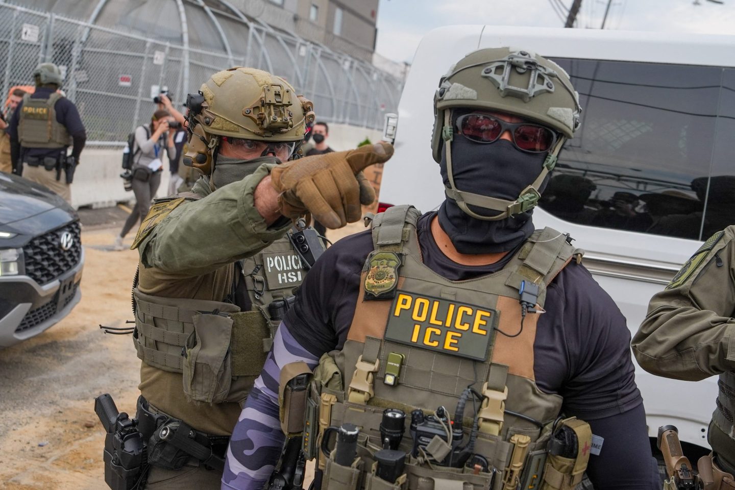 Two ICE agents wearing camouflage gear with eye and face coverings.