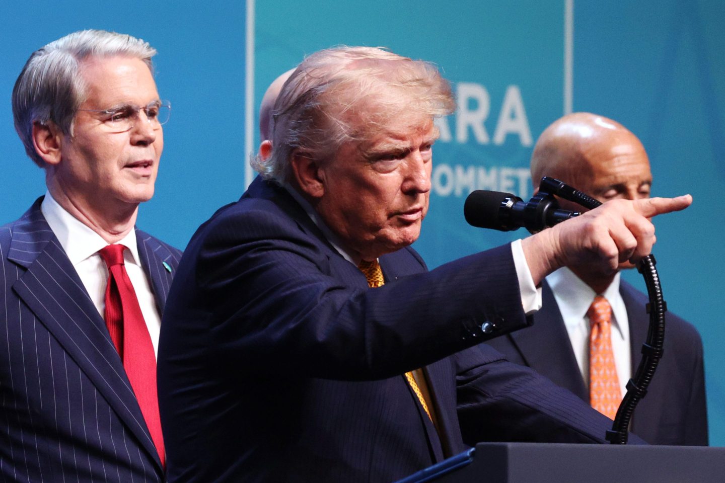 Donald Trump, standing behind a podium, points in front of him with Scott Bessent standing behind him.