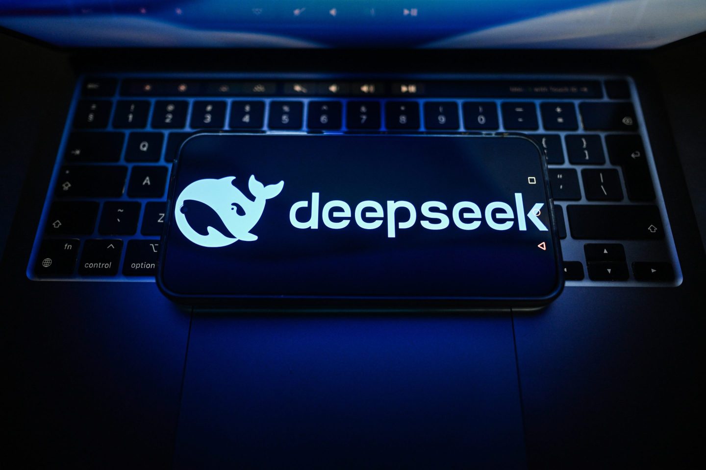 A DeepSeek logo is seen displayed on a smartphone on the top of a laptop.