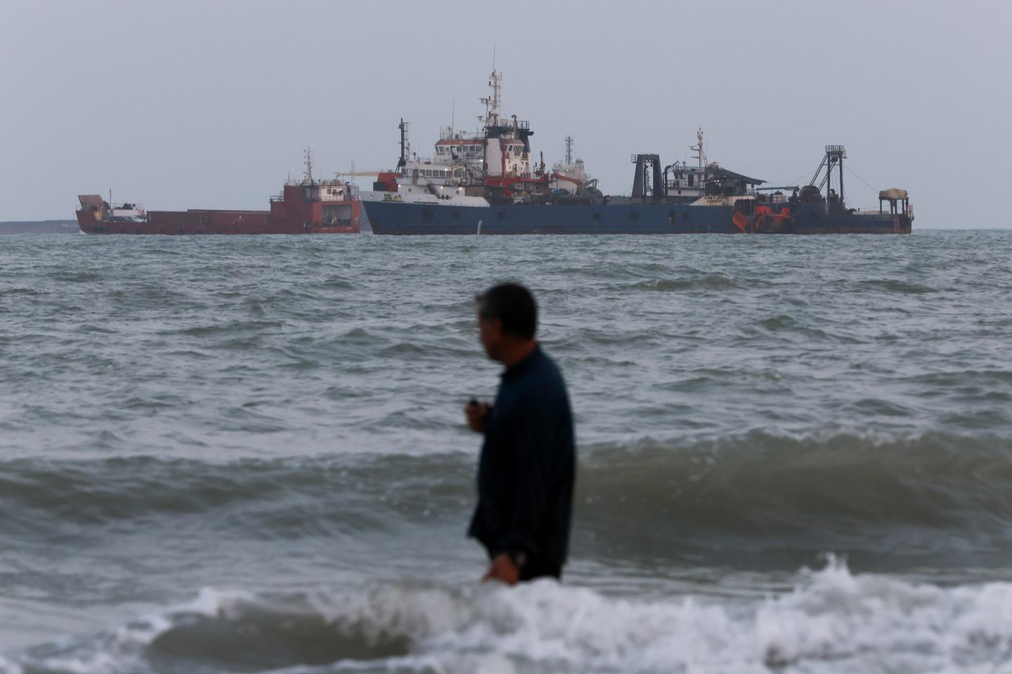 BANDAR ABBAS, IRAN - A person wades in the water as ships are seen anchored in the Strait of Hormuz on Aug. 10, 2026 off the coast of Bandar Abbas, Iran. In a recent statement, Iran's Supreme National Security Council said the vital waterway would not reopen until the United States corrects its behavior, demanding that the U.S. end its war on Iran and compensate the country for war damage, among other conditions. Iran has largely halted vessel traffic through the strait with the threat of strikes; meanwhile, the U.S. has imposed a blockade on Iranian ports.