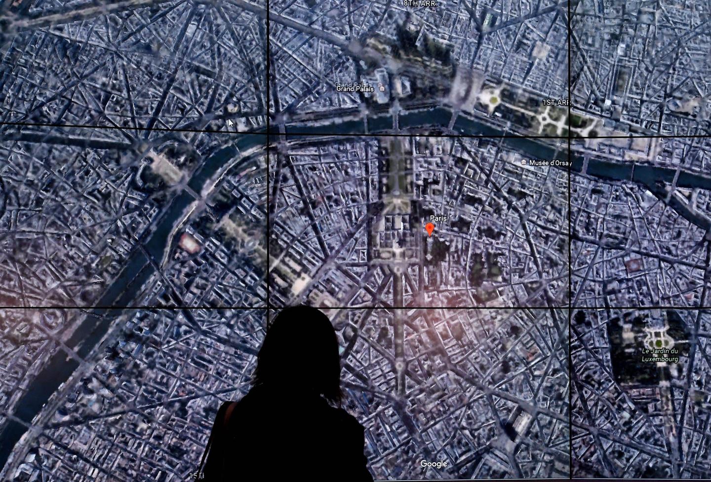 People look at a Google Earth map of Paris,France on a screen as Google Earth.