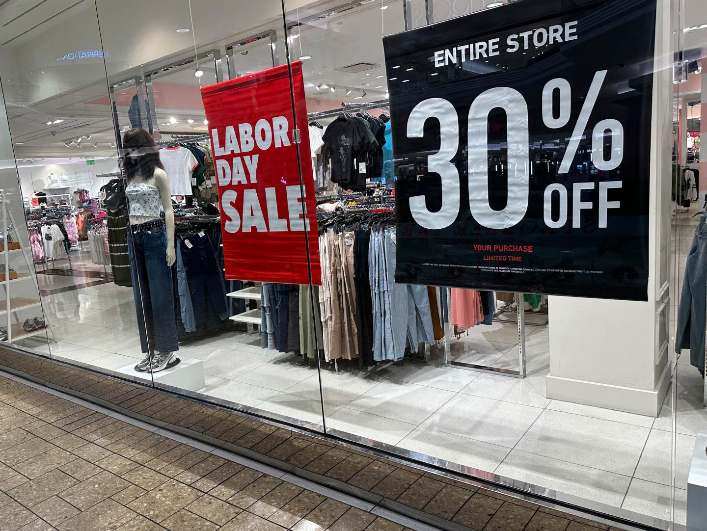 Signs announce a Labor Day sale in the window of a clothing store at a mall in Denver on Aug. 21, 2024.