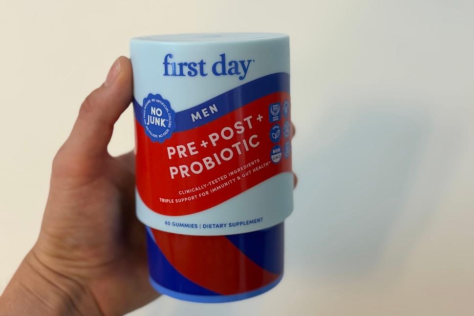 Closeup of a hand holding a canister of First Day Men's 3-in-1 Pre+ Post+ Probiotic gummies
