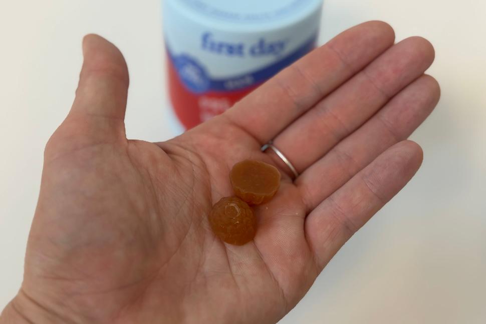 Closeup of an open palm holding two First Day Men's 3-in-1 Pre+ Post+ Probiotic gummies. You can see the open gummy canister on the white countertop below.
