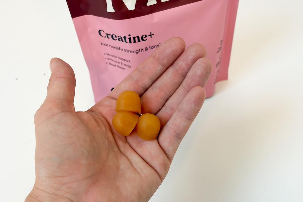 Closeup of an open palm holding three Midi Creatine+ gummies. The bag of gummies can be seen on the white countertop below.