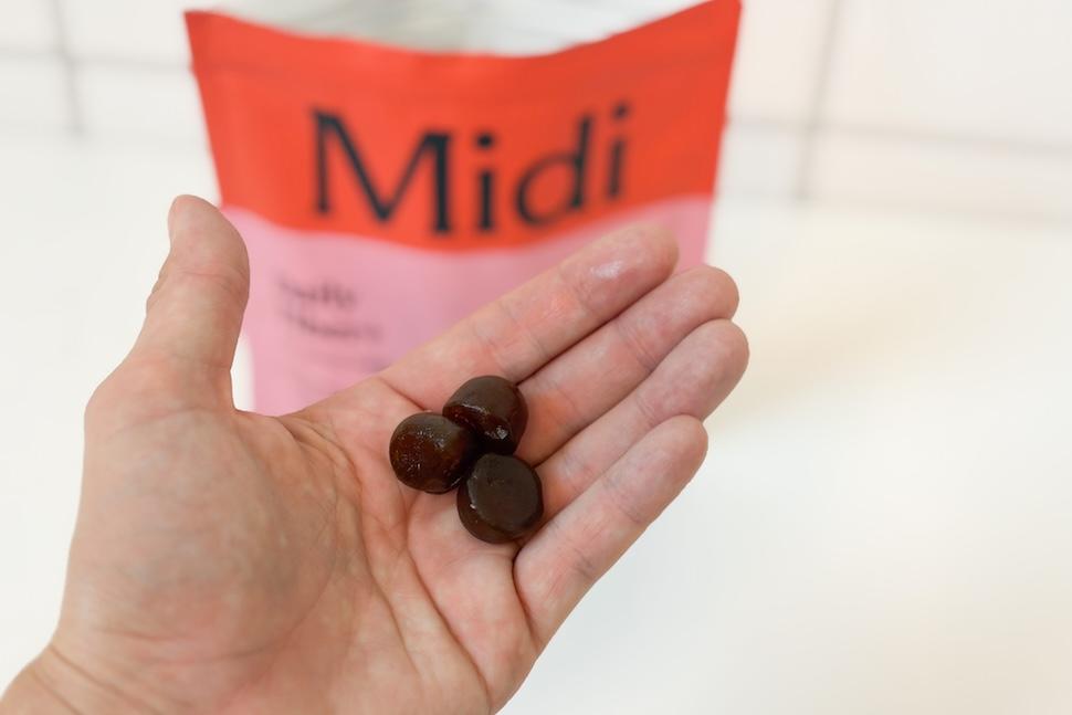 A closeup of a hand holding three Midi Daly Fiber+ gummies. You can see the open bag of gummies on the countertop below.