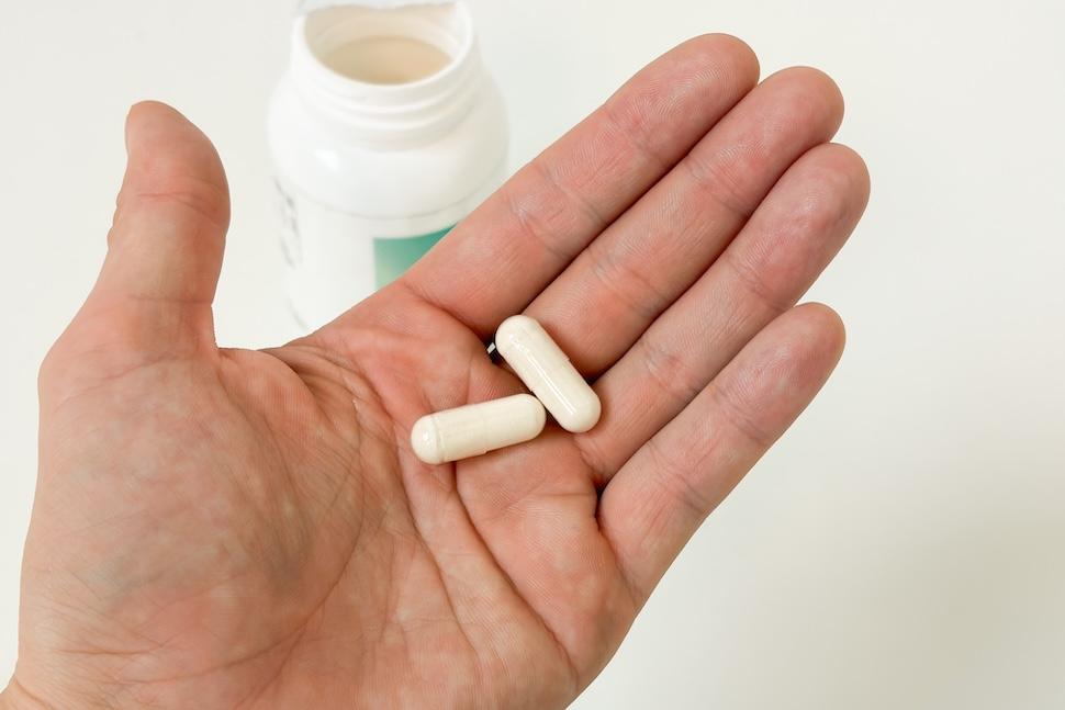 An open palm holding two off-white Performance Lab Prebiotic pills. You can see the open pill bottle below on a white countertop.