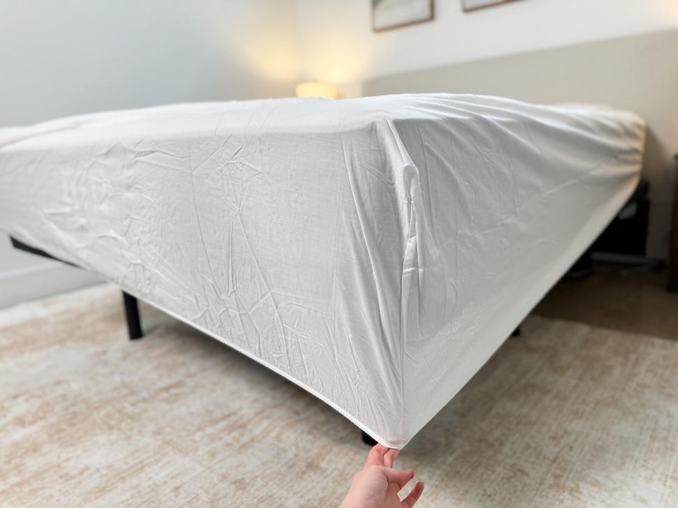 Closeup of a hand tugging down the corner of the Silk & Snow Pecale Bed Sheets over a mattress