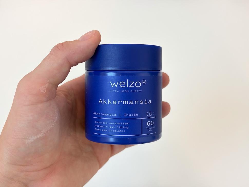 Closeup of a hand holding a blue bottle of Welzo Akkermansia