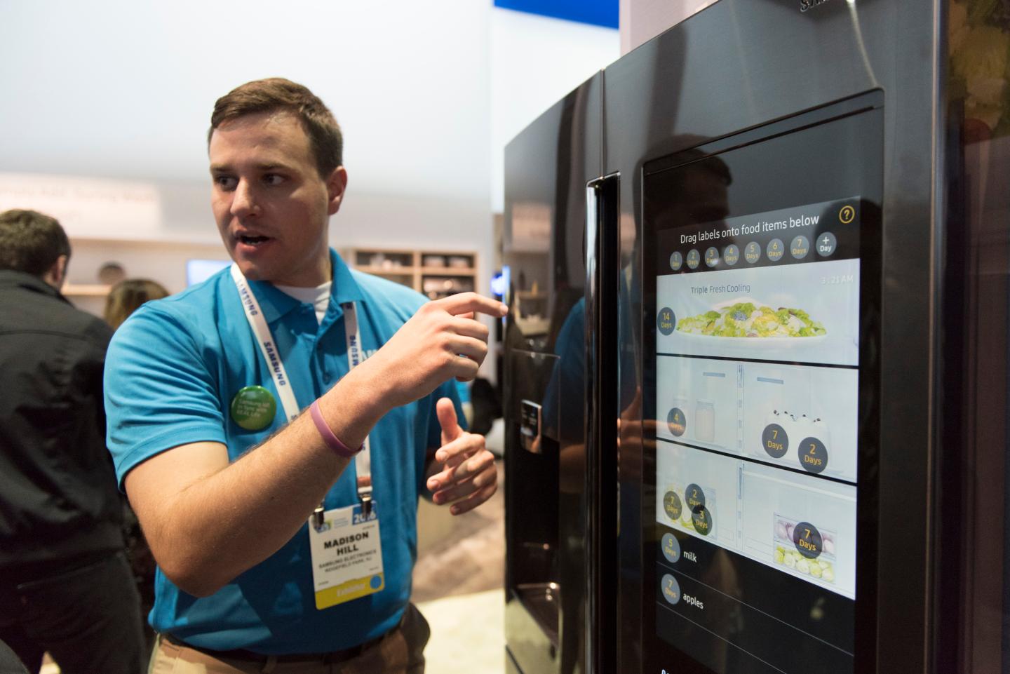A man in a blue short points to the display screen on a Samsung refrigerator.